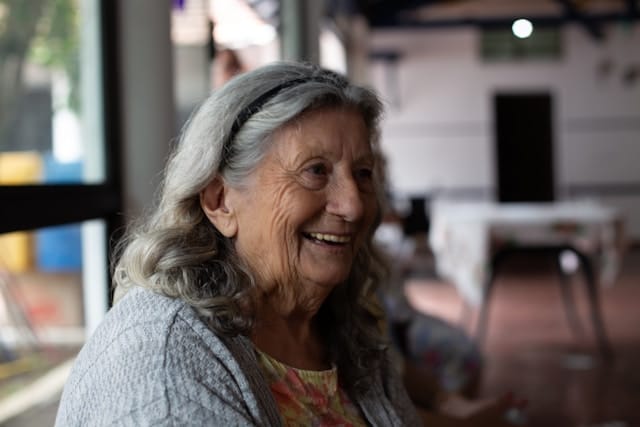 Une femme âgée sourit dans un intérieur chaleureux.