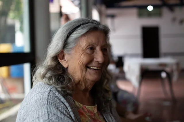 Une femme âgée sourit dans un intérieur chaleureux.