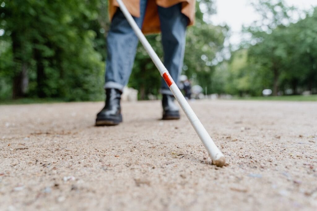 Personne utilisant une canne blanche sur chemin de terre.