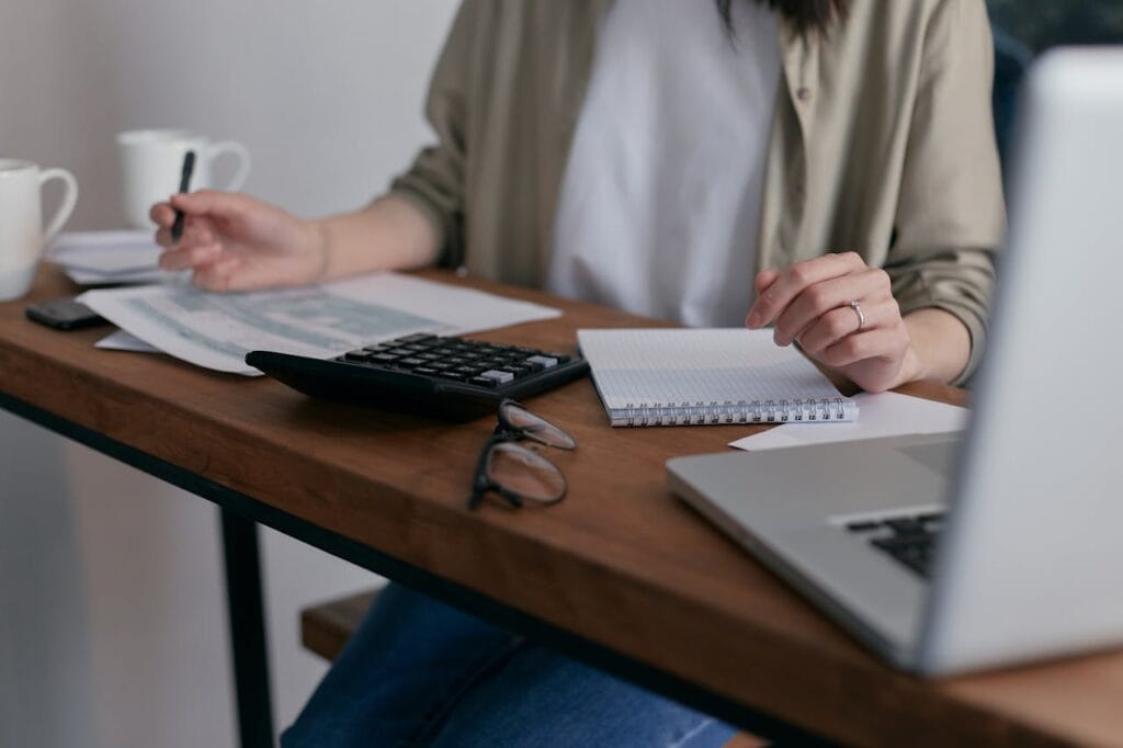 Calculatrice, documents et ordinateur sur bureau en bois.