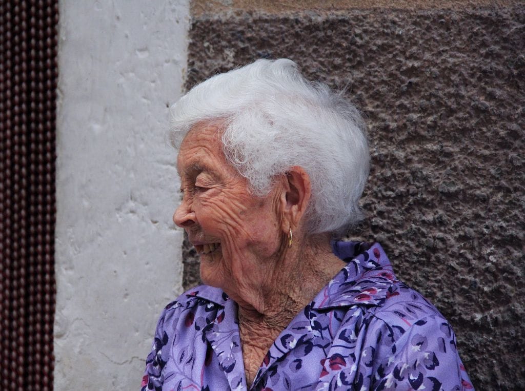 Personne âgée souriante en extérieur.