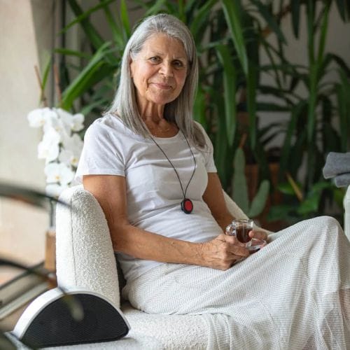 Femme âgée assise avec café en intérieur végétal.