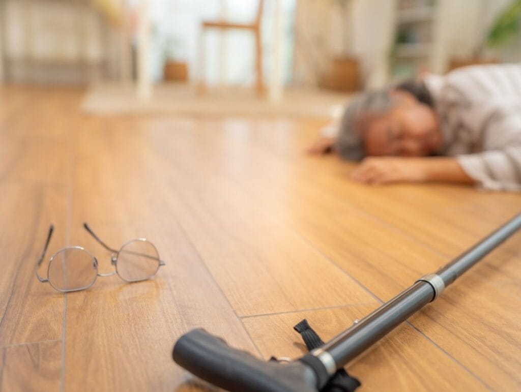 Personne âgée tombée au sol avec canne et lunettes.