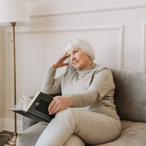Femme âgée lisant sur un canapé beige.