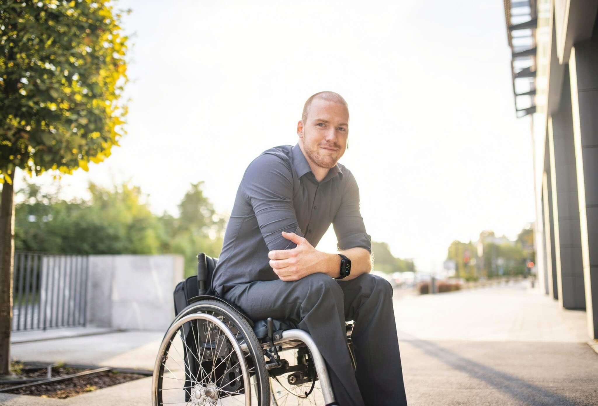 Homme souriant en fauteuil roulant dehors.