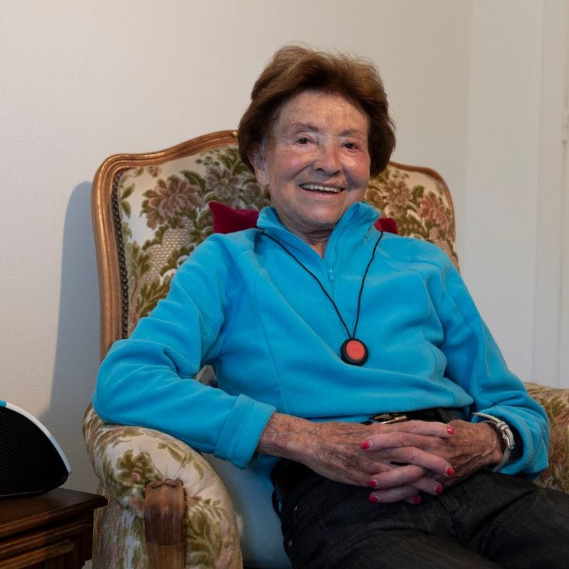 Personne âgée souriante dans un fauteuil floral.