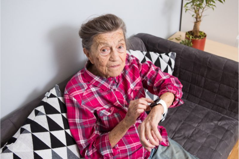 Personne âgée vérifiant une montre connectée sur un canapé.